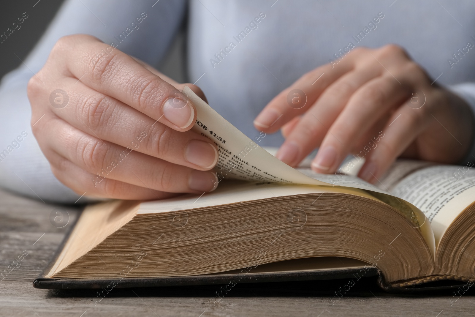 Photo of Woman reading Bible at wooden table, closeup