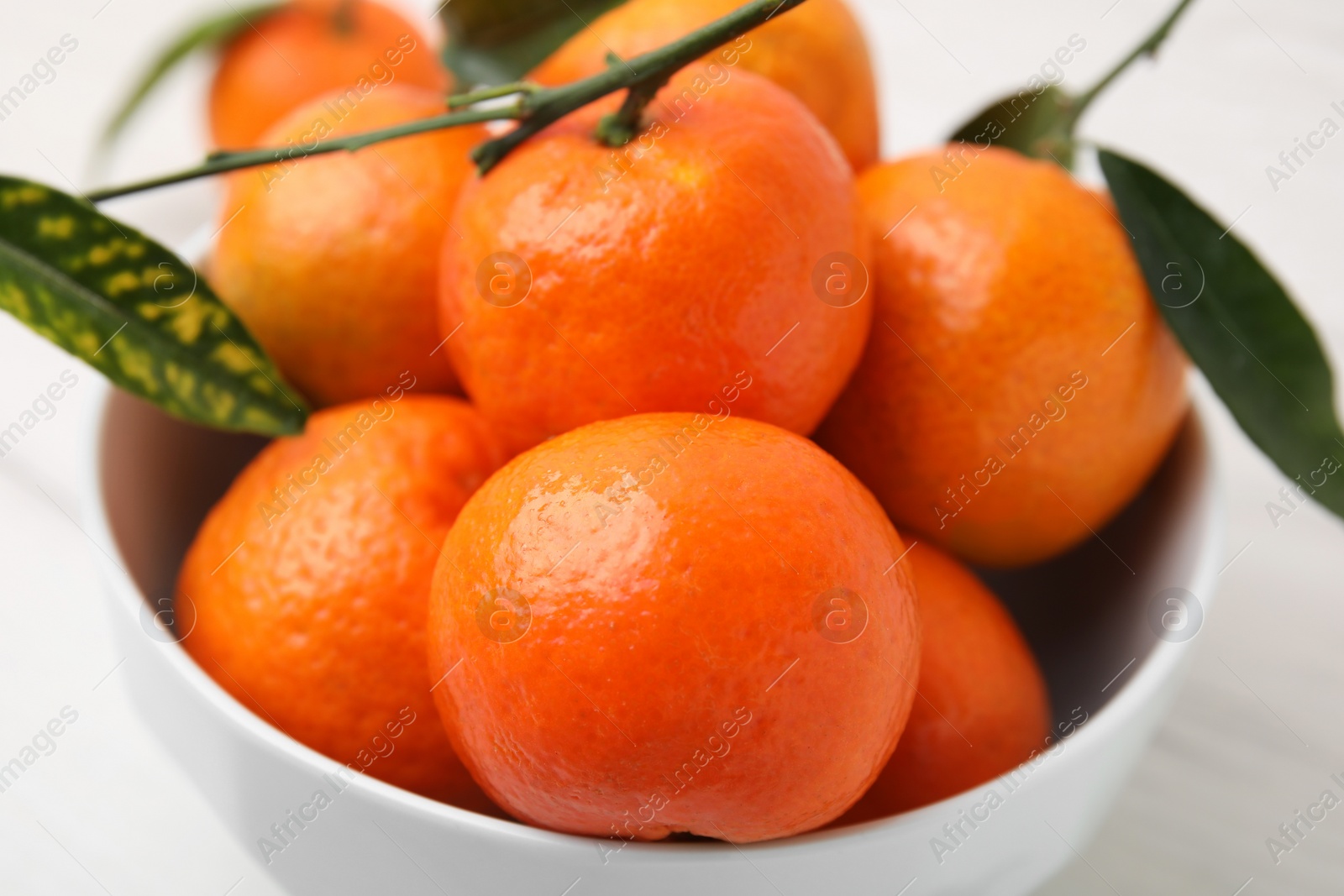 Photo of Fresh ripe tangerines and leaves in bowl on white table, closeup