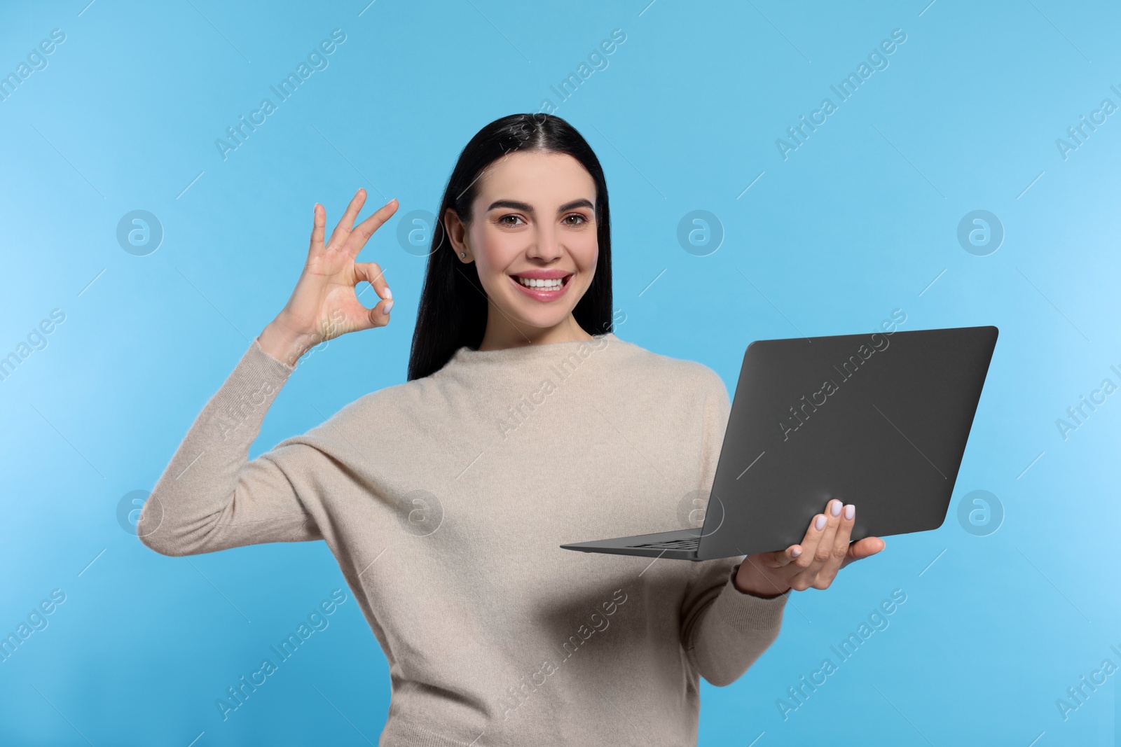 Photo of Happy woman with laptop showing okay gesture on light blue background