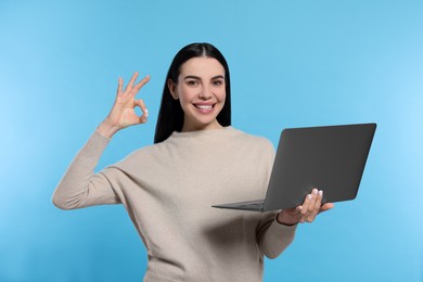 Photo of Happy woman with laptop showing okay gesture on light blue background