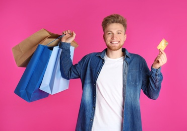 Photo of Young man with credit card and shopping bags on color background. Spending money
