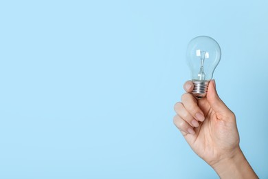 Photo of Woman holding incandescent light bulb on blue background, closeup. Space for text
