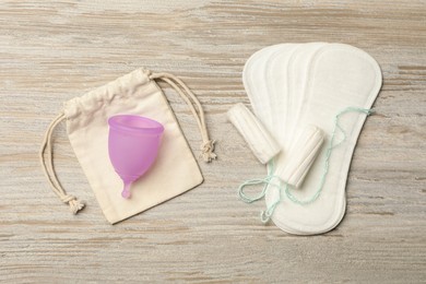 Menstrual cup with bag, pantyliners and tampons on wooden background, flat lay