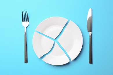 Photo of Pieces of broken ceramic plate and cutlery on light blue background, flat lay