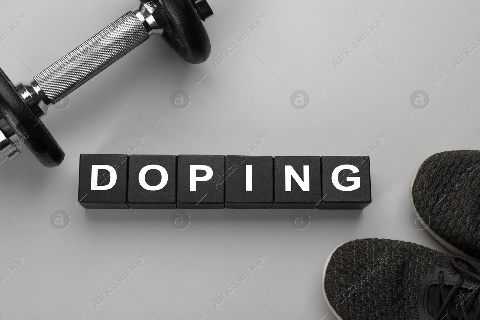 Photo of Black wooden cubes with word Doping, dumbbell and sport shoes on light grey background, flat lay