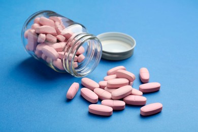 Photo of Bottle of pink vitamin capsules on blue background