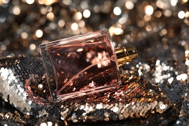 Luxury perfume in bottle on fabric with shiny sequins, closeup