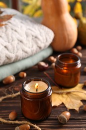 Burning scented candles, warm sweaters and acorns on wooden table. Autumn coziness