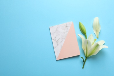 Image of Beautiful lily and notebook on light blue background, flat lay. Space for text