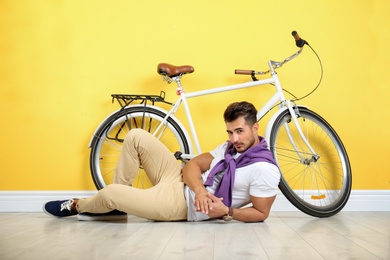 Photo of Handsome young hipster man lying with bicycle near yellow wall