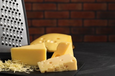 Photo of Grated, cut cheese and grater on black table. Space for text