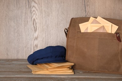 Photo of Postman's hat near bag full of letters on wooden background. Space for text