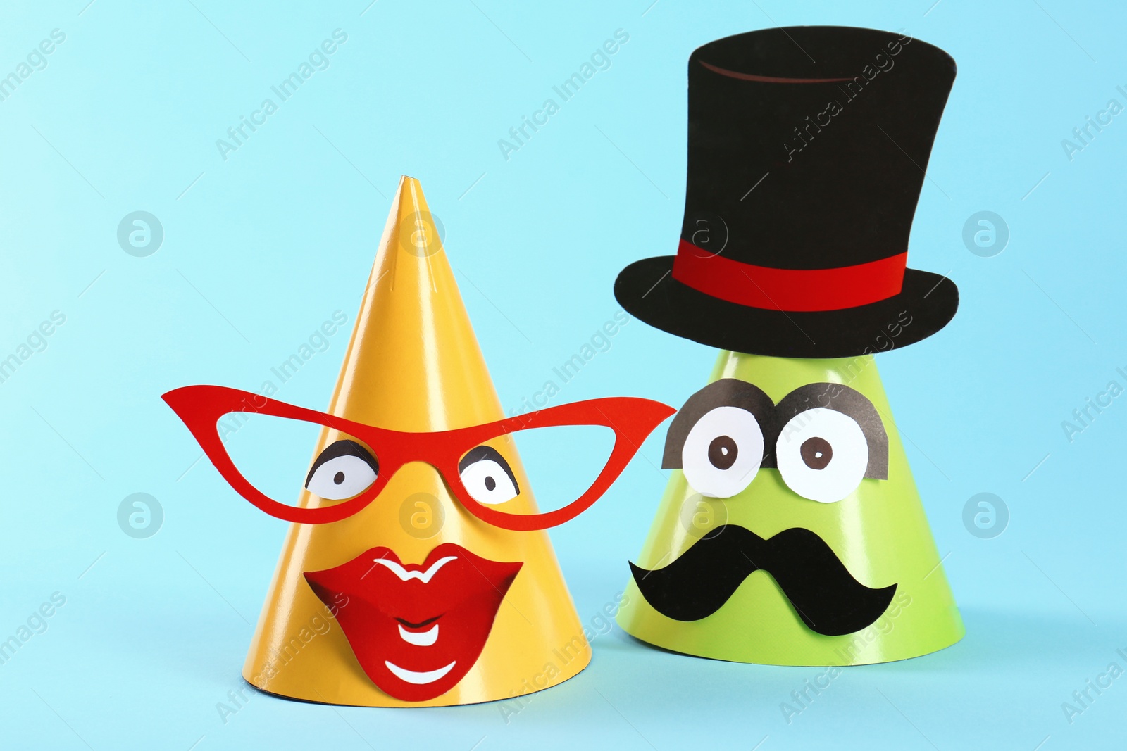 Photo of Handmade party hats with funny faces on light blue background