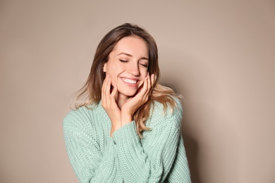 Image of Happy young woman wearing warm sweater on beige background 