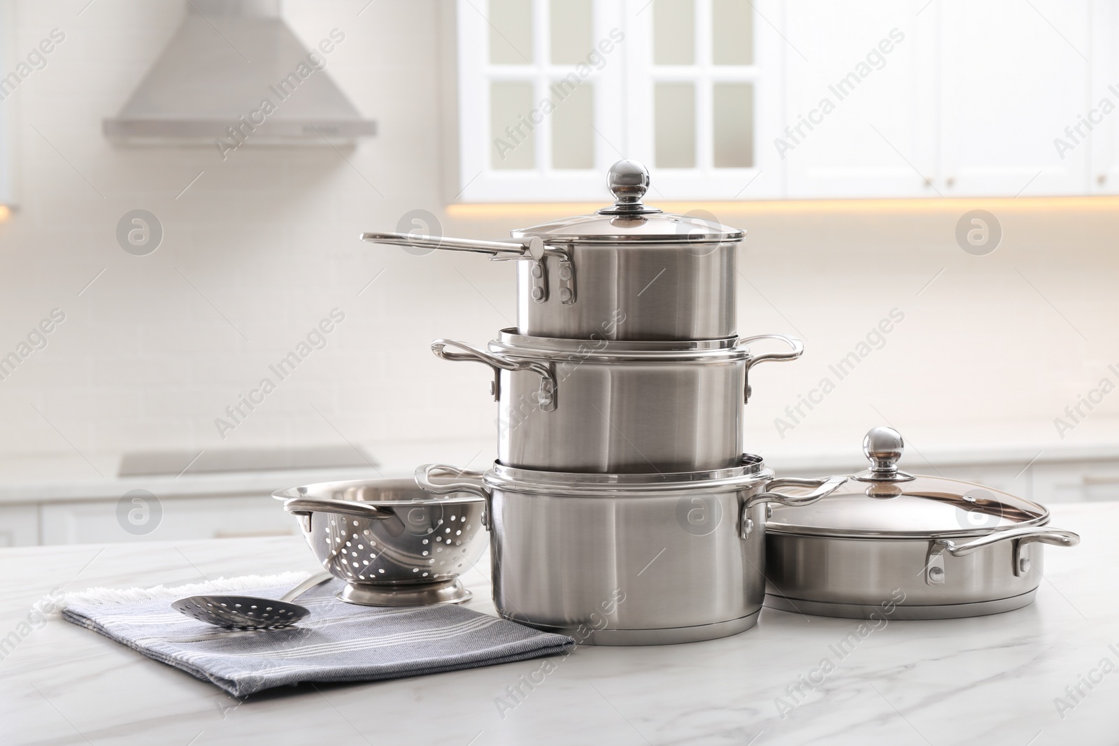 Photo of Set of stainless steel cookware and kitchen utensils on white table indoors