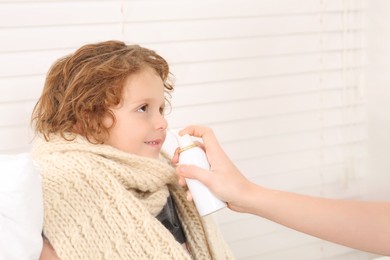 Mother using nasal spray to treat her little son indoors, closeup