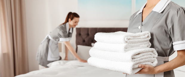 Chambermaid holding stack of fresh towels in hotel room, closeup view with space for text. Banner design