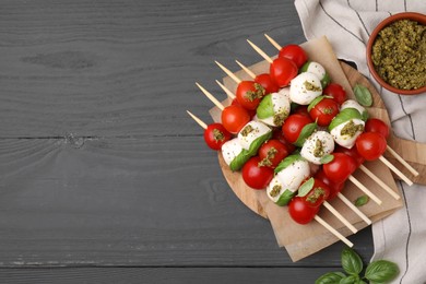 Photo of Caprese skewers with tomatoes, mozzarella balls, basil and pesto sauce on grey wooden table, flat lay. Space for text