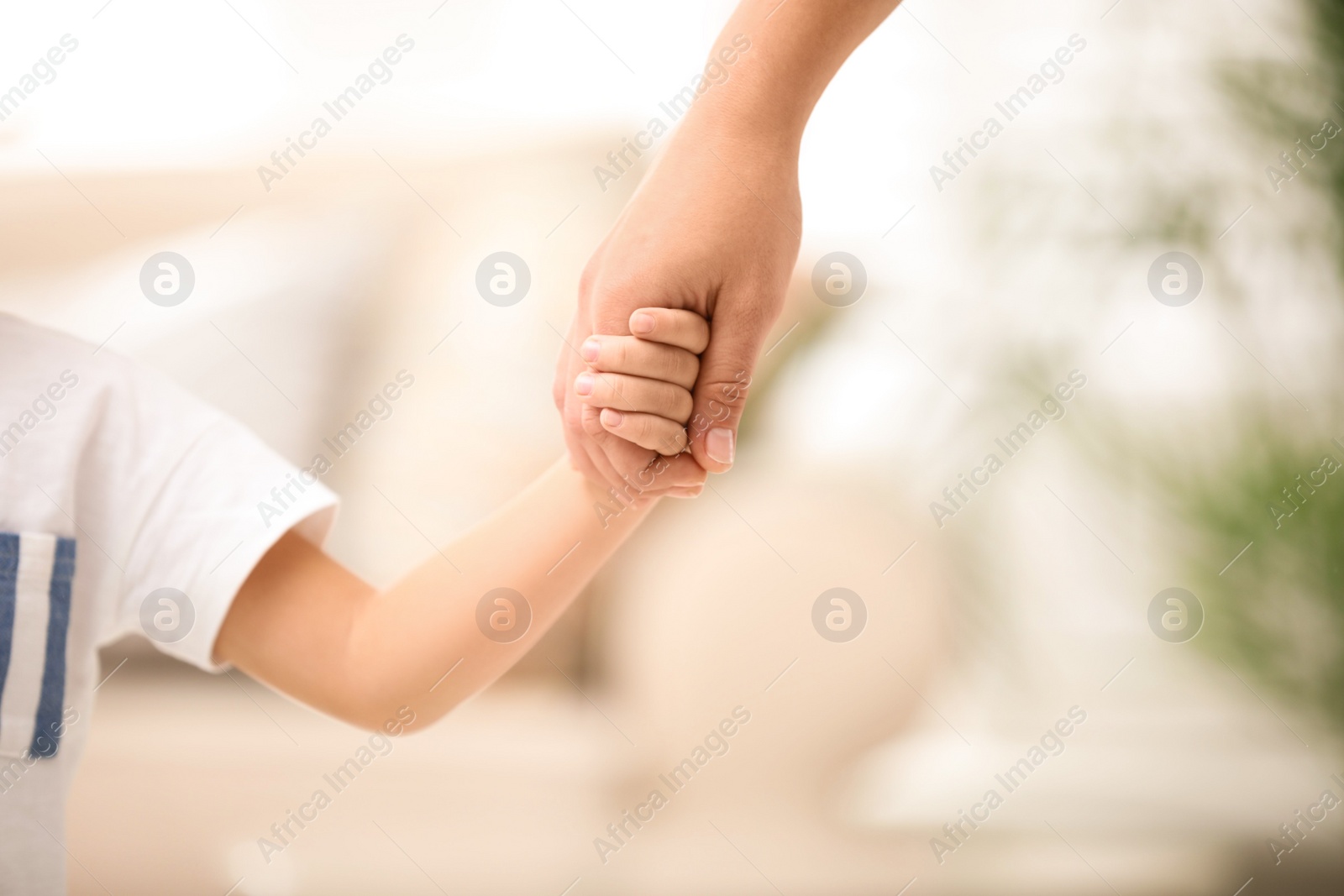 Photo of Mother holding hands with her child indoors, closeup. Happy family