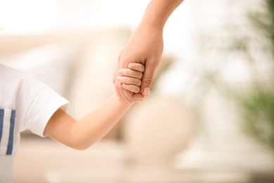 Mother holding hands with her child indoors, closeup. Happy family