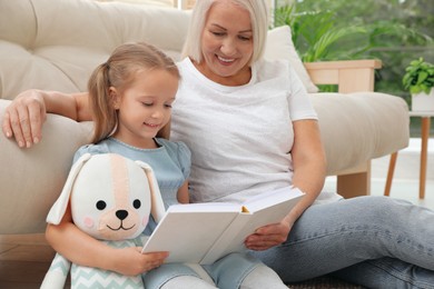 Happy grandmother with her granddaughter reading book together at home