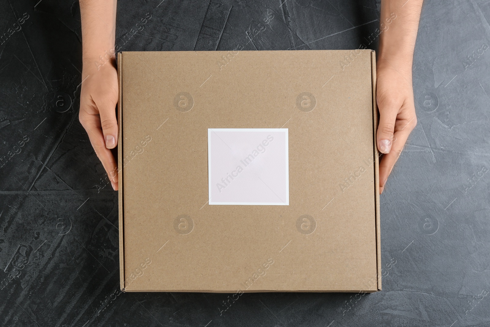 Photo of Woman holding cardboard box at grey stone table, top view