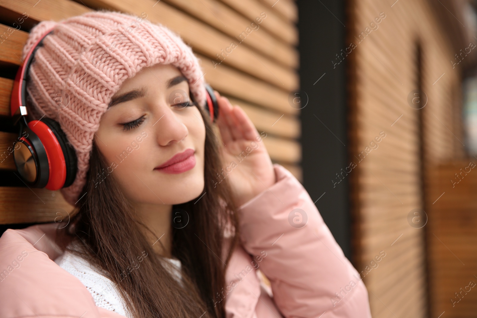 Photo of Young woman listening to music with headphones near wooden wall. Space for text