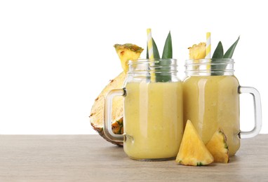 Photo of Tasty pineapple smoothie in mason jars and sliced fruit on wooden table against white background. Space for text