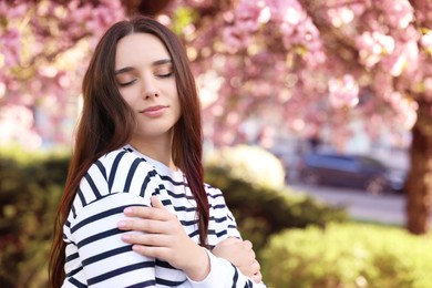 Beautiful woman near blossoming tree on spring day, space for text