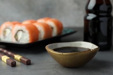 Photo of Tasty soy sauce, chopsticks and sushi rolls with salmon on grey table, closeup