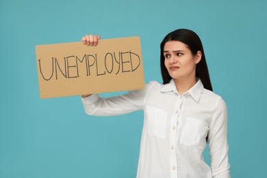 Photo of Unhappy woman holding sign with word Unemployed on light blue background