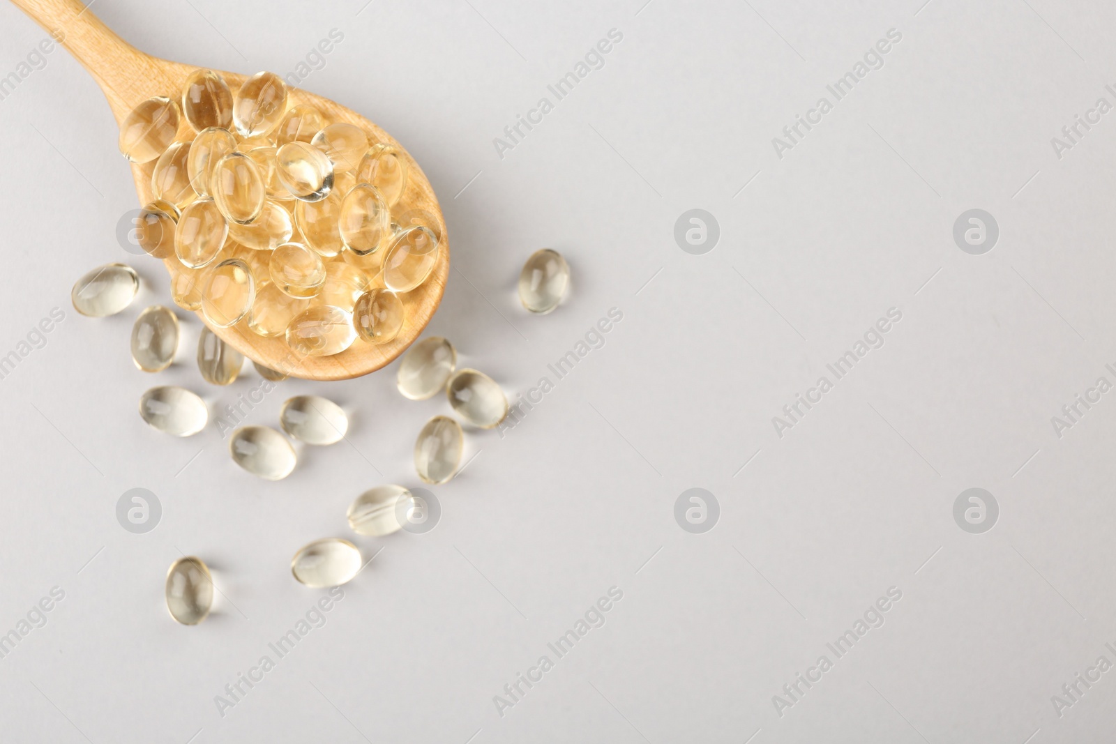 Photo of Wooden spoon with vitamin capsules on light background, top view. Space for text