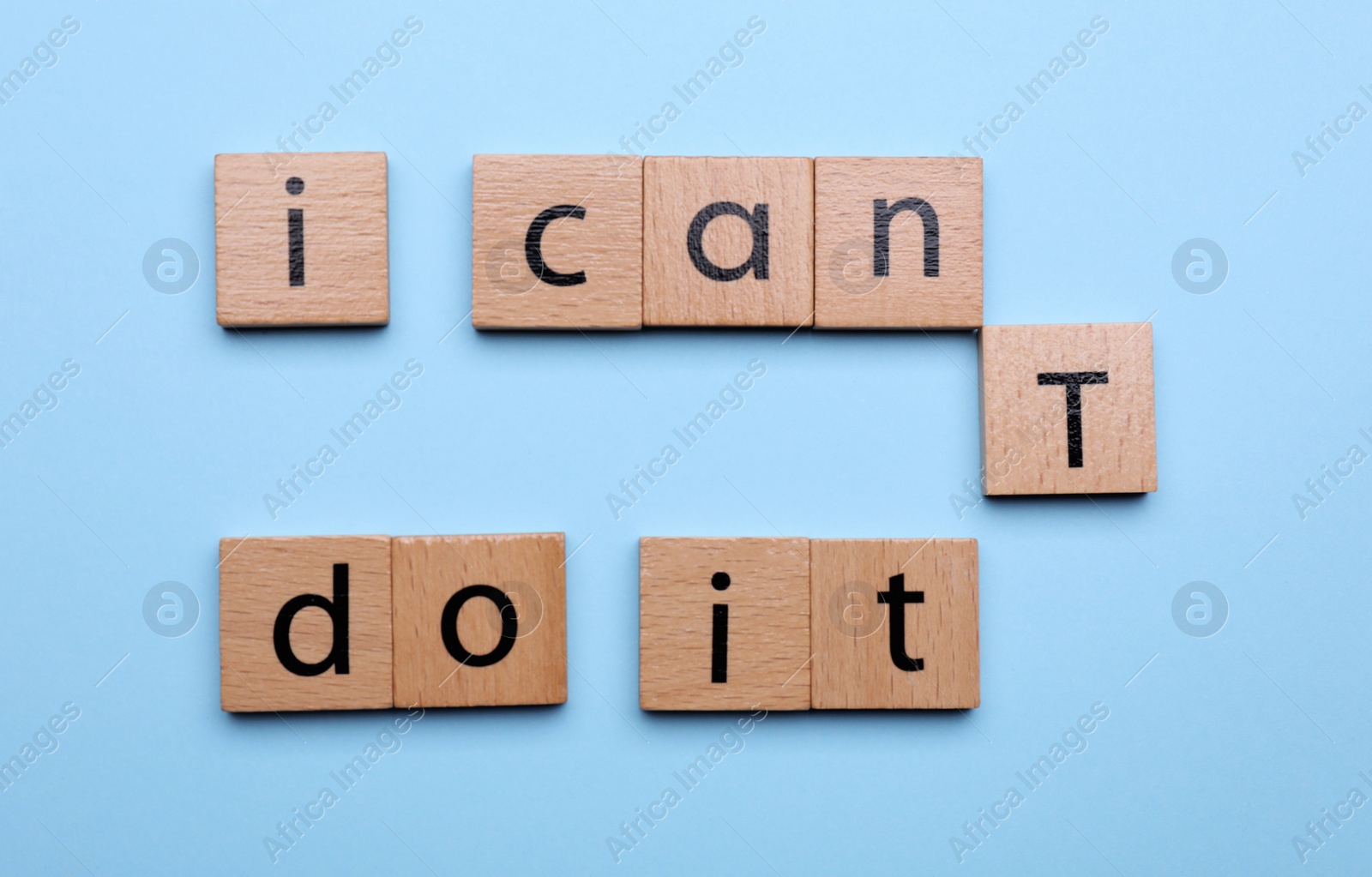 Photo of Motivation concept. Changing phrase from I Can't Do It into I Can Do It by removing wooden square with letter T on light blue background, flat lay