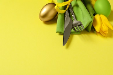 Photo of Cutlery set, painted eggs and beautiful flower on yellow background, space for text. Easter celebration
