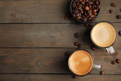 Photo of Cups of hot aromatic coffee and roasted beans on wooden table, flat lay. Space for text