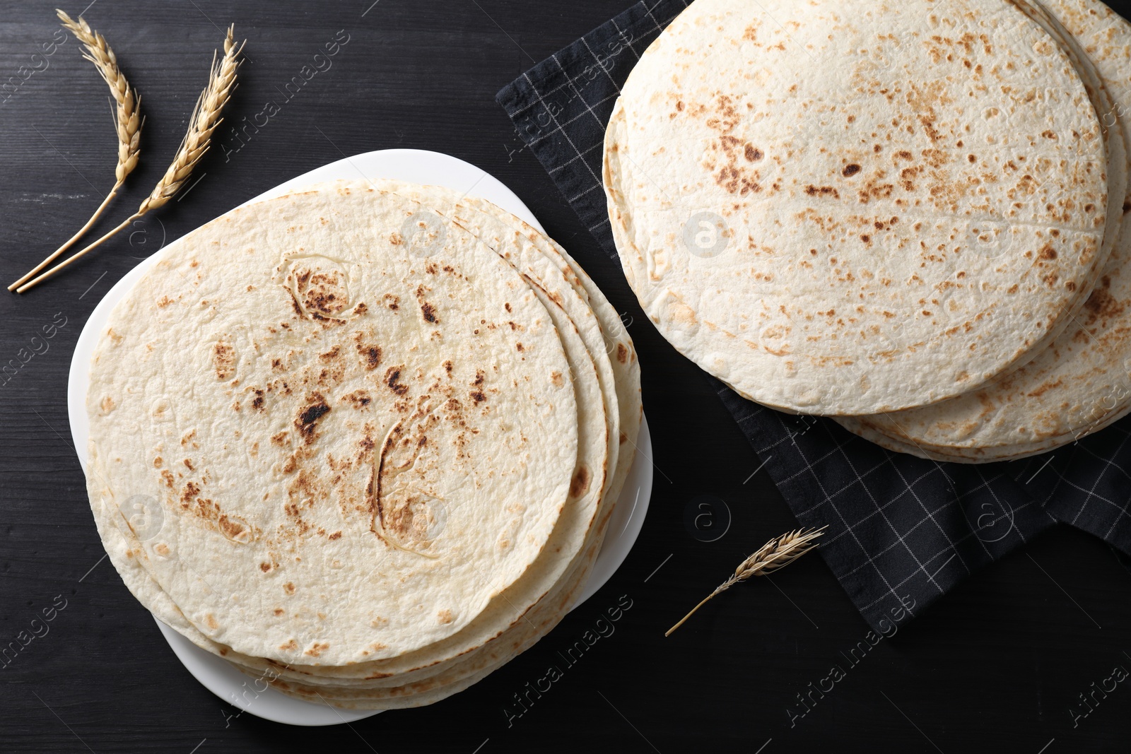 Photo of Many tasty homemade tortillas on black wooden table, top view