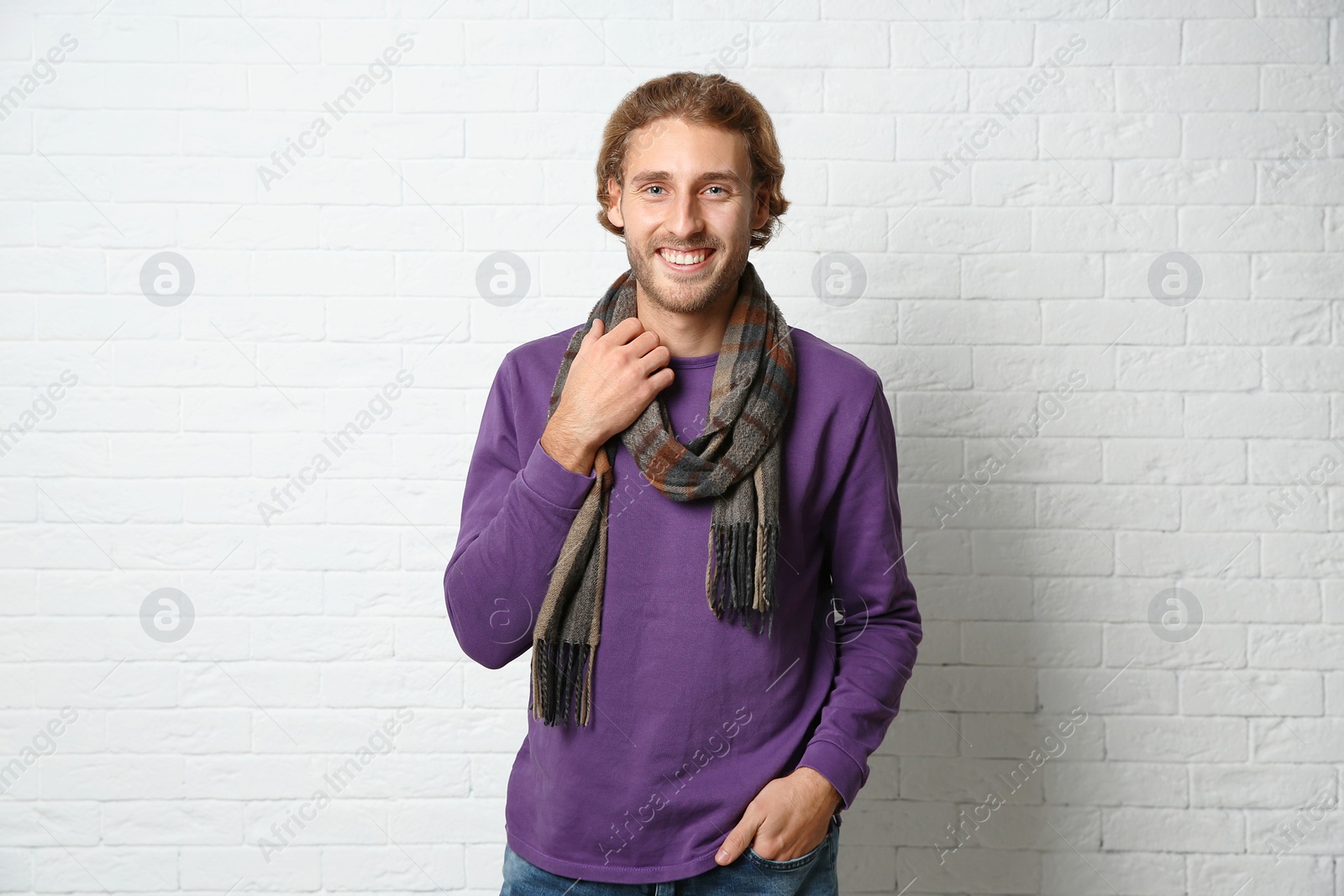 Photo of Handsome young man in warm sweater with scarf near white brick wall