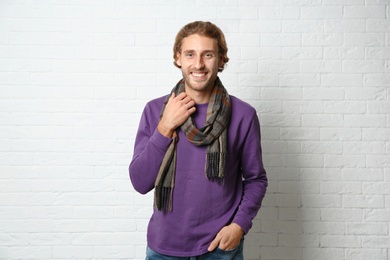 Handsome young man in warm sweater with scarf near white brick wall