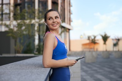 Beautiful woman in stylish sportswear listening music on city street, space for text