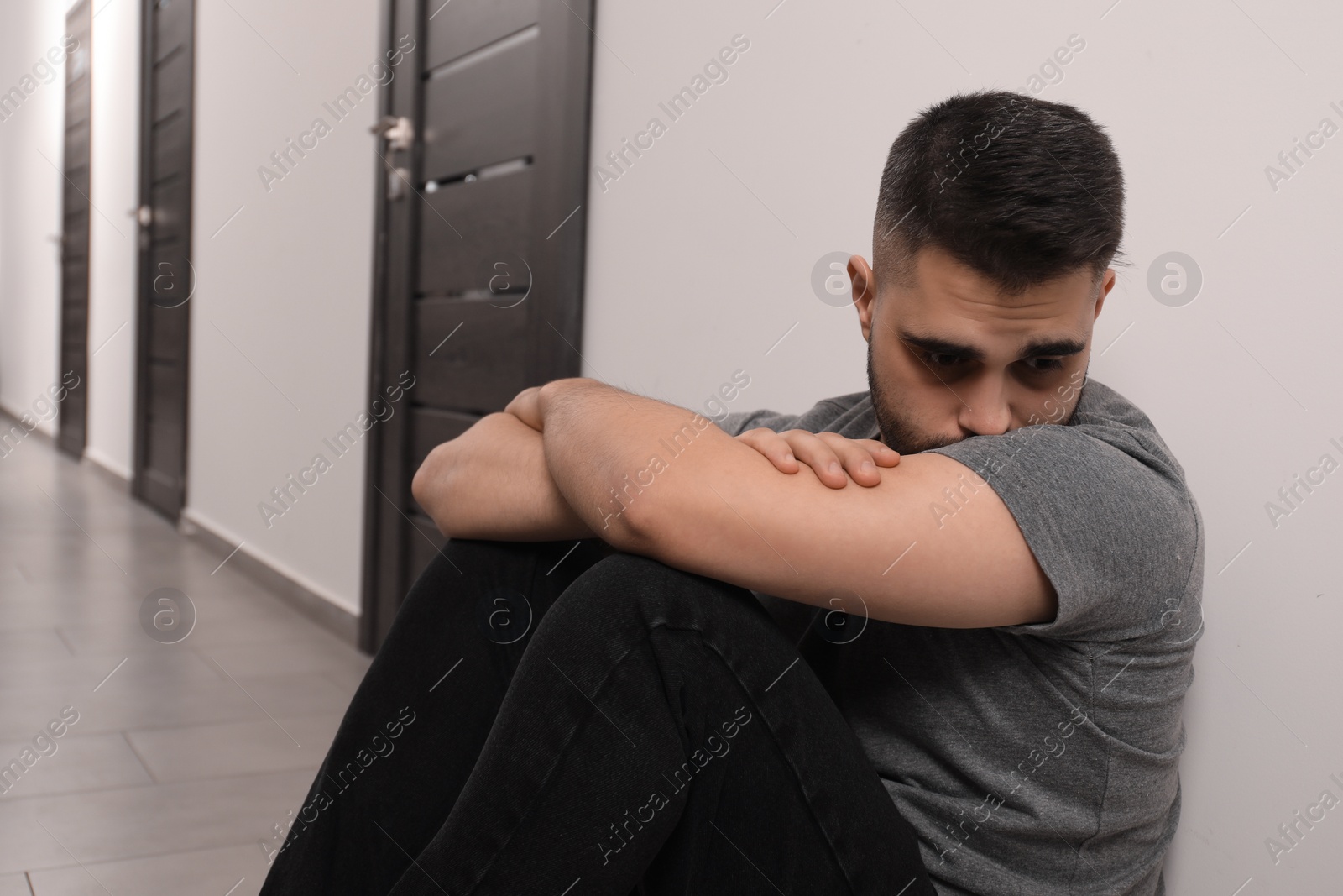 Photo of Sad man sitting on floor in hall. Space for text