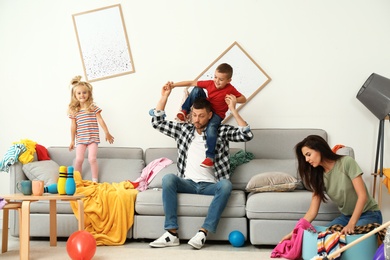 Frustrated mother trying to clean up mess while father playing with children in room