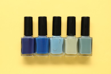 Photo of Bright nail polishes in bottles on yellow background, flat lay