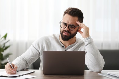 Photo of Man with glasses suffering from headache at workplace in office