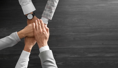 Photo of People holding hands together over grey wooden background, top view with space for text. Unity concept