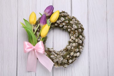 Photo of Wreath made of beautiful willow, colorful tulip flowers and pink bow on white wooden background, top view