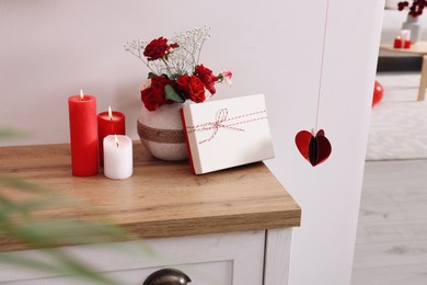 Photo of Vase with beautiful flowers, gift box and candles on wooden table indoors. Happy Valentine's Day