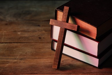 Photo of Cross and stack of books on wooden table, closeup with space for text. Religion of Christianity