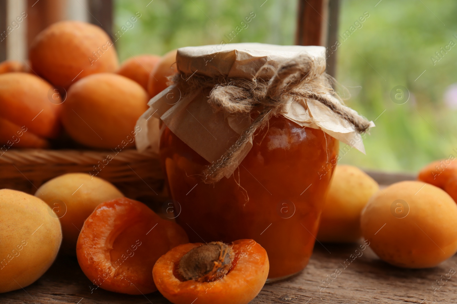 Photo of Jar of delicious jam and fresh ripe apricots on wooden table indoors. Fruit preserve