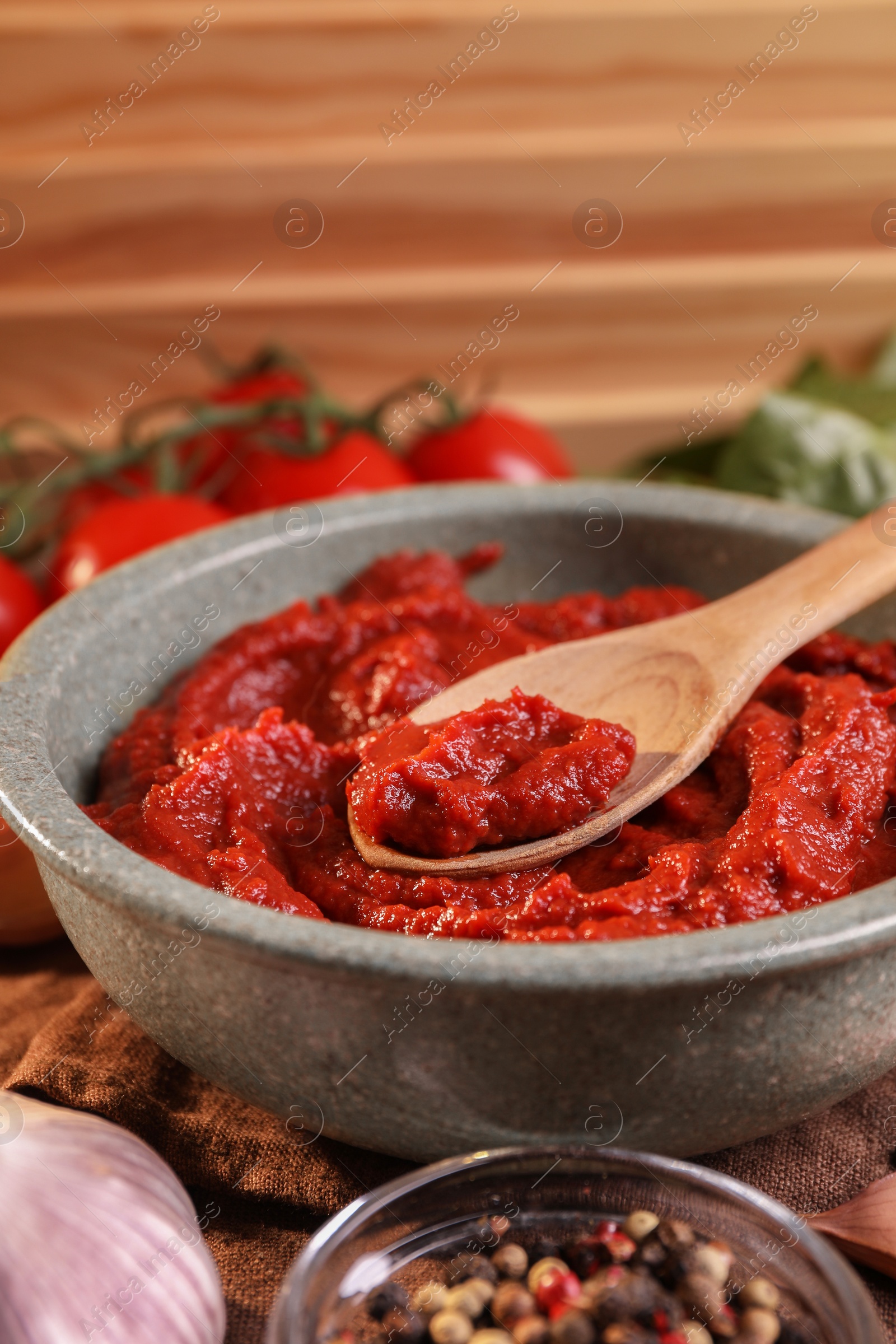 Photo of Bowl of tasty tomato paste with spoon and ingredients on table