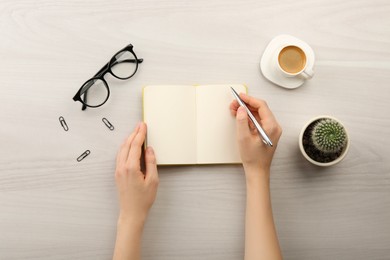 Photo of Woman writing in notebook at light wooden table, top view